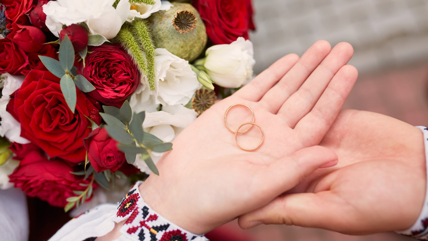 Bride and groom hold wedding rings in their arms